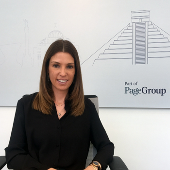Mujer sentada frente a un poster de PageGroup, sonriendo.