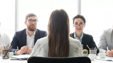 Una persona de espaldas en una entrevista con cuatro personas sentadas en la mesa.