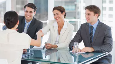 Grupo de personas en una reunión, dos estrechan manos.