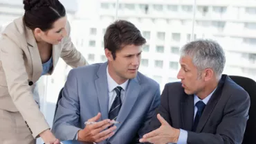 Tres personas discutiendo en una reunión de negocios.