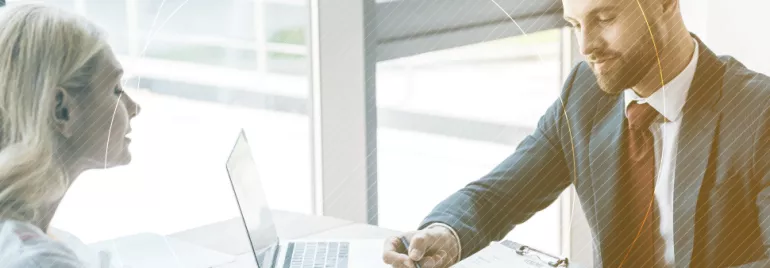 Dos personas conversan en una oficina con una laptop abierta.