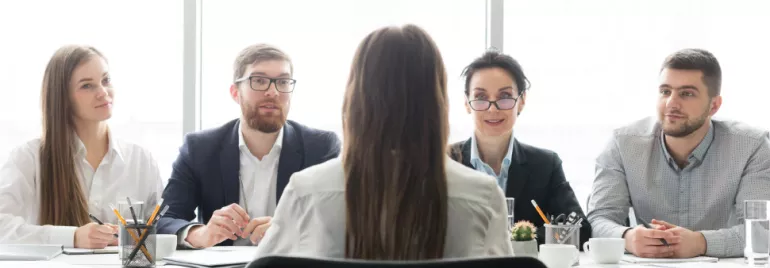 Una persona de espaldas en una entrevista con cuatro personas sentadas en la mesa.