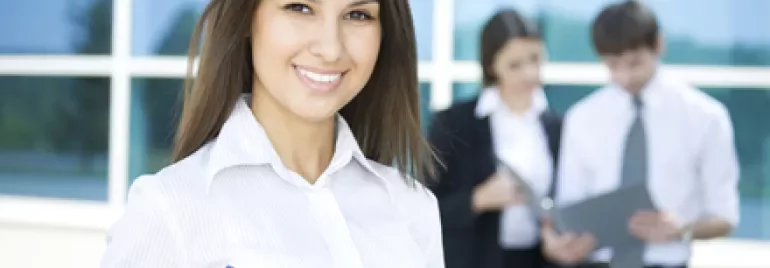 Persona sonriente con una carpeta azul, con dos personas trabajando atrás.