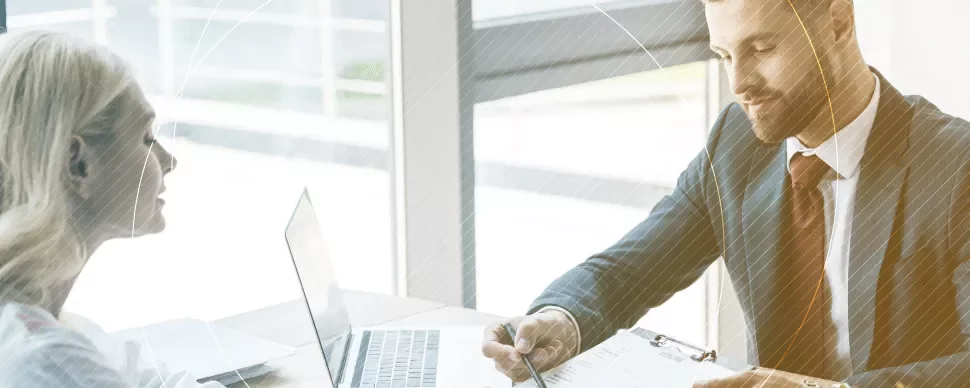 Dos personas conversan en una oficina con una laptop abierta.