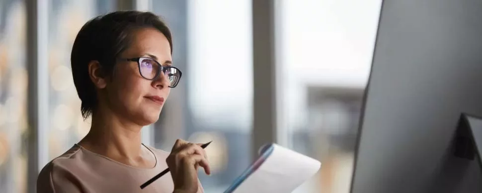 Persona leyendo notas frente a una computadora en oficina.