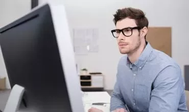 Persona trabajando en un ordenador, vestido con una camisa azul.