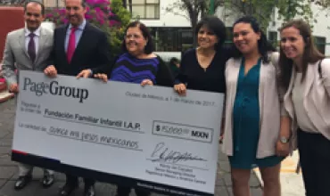 Grupo de personas posando con un cheque grande al aire libre.