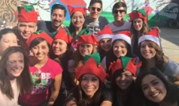 Grupo de personas con gorros navideños posando y sonriendo al aire libre.