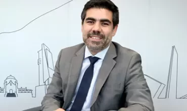 Persona sonriendo, sentada en una mesa, fondo de diseño arquitectónico.