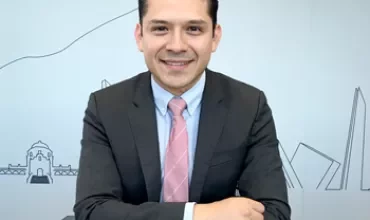 Persona con traje y corbata sonriente, sentado en una mesa.